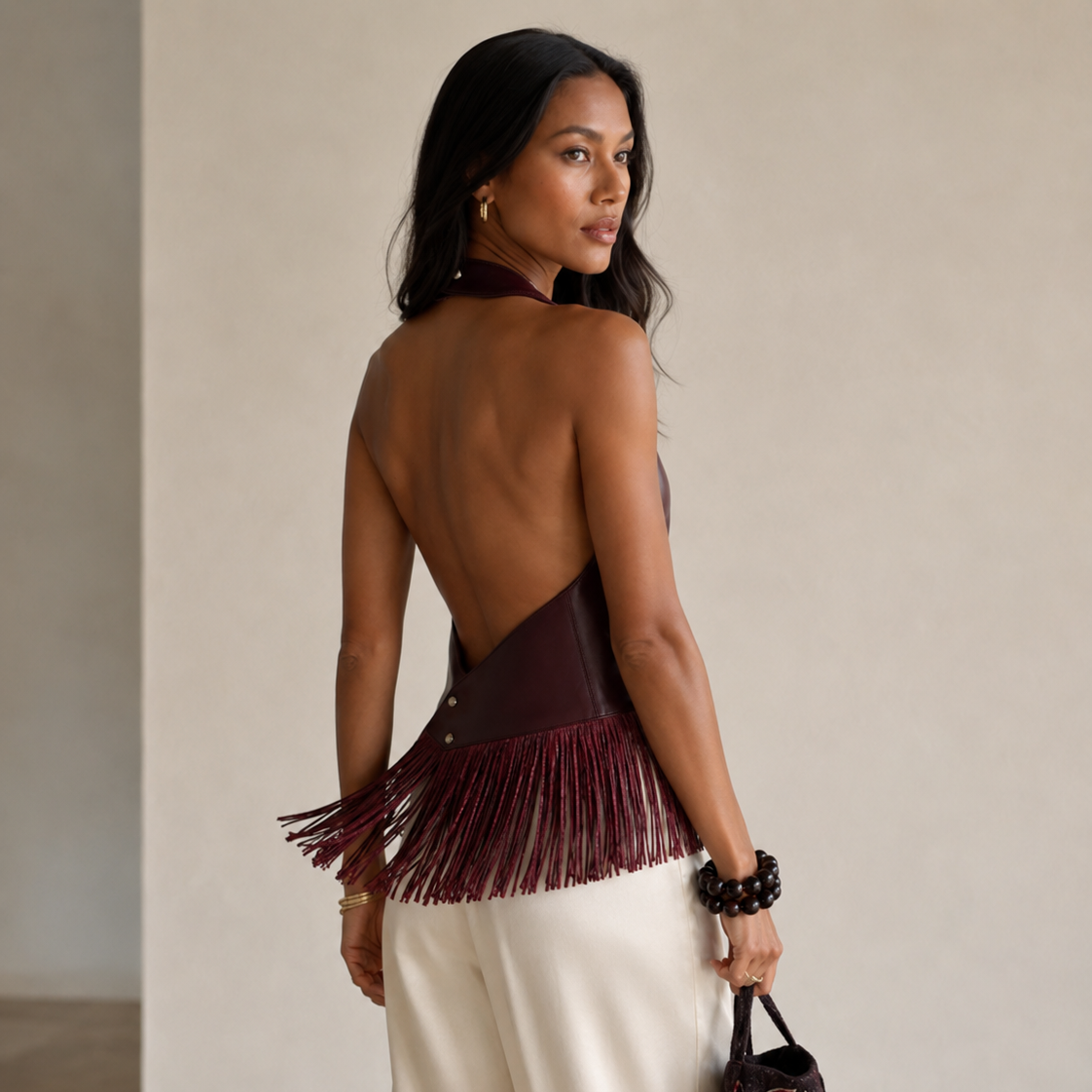 Woman wearing a backless top with fringe details and holding a handbag.