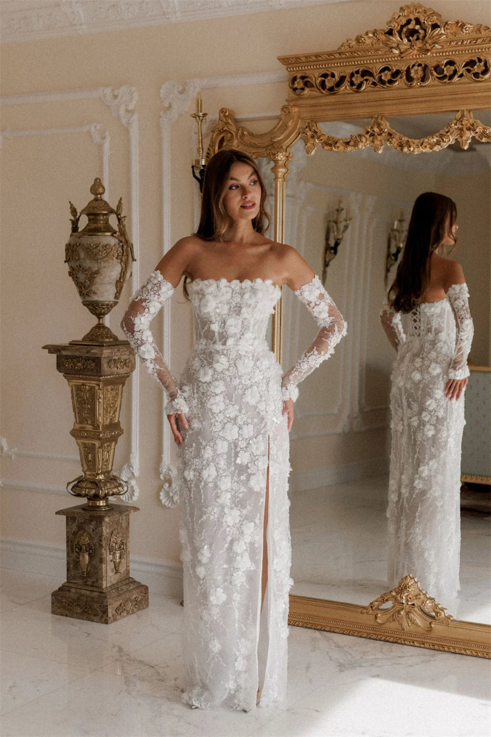 Woman in a white lace wedding dress standing in front of a large ornate mirror.
