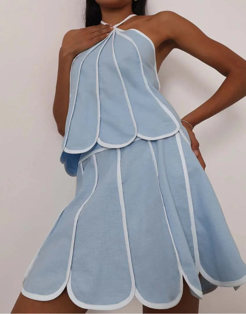 Woman wearing a light blue halter dress with white trim against a plain background