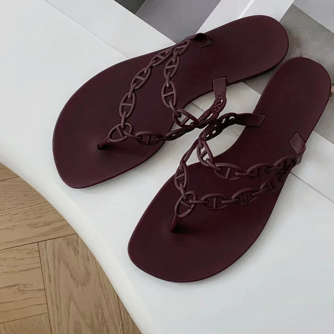 Pair of maroon sandals with braided straps on a white surface.