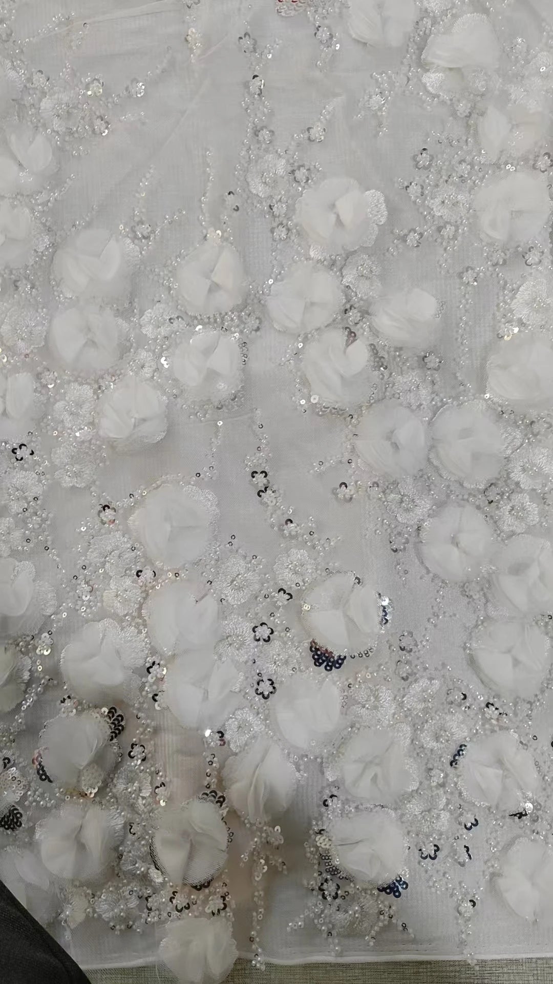 Close-up of a textured white fabric with floral patterns and small embellishments.