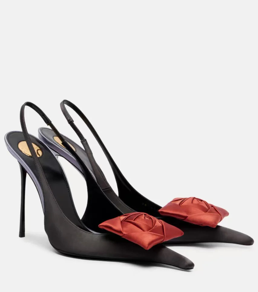 Black high-heeled shoes with red bow details on a light gray background