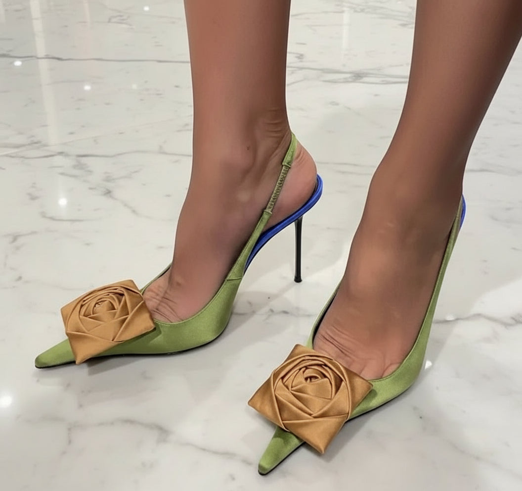 Green high-heeled shoes with brown rose decorations on a gray floor.