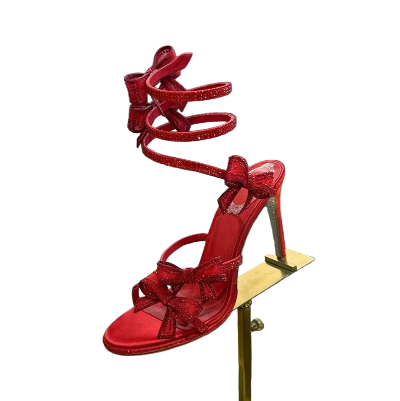 Red glittery high-heeled sandals on a metallic stand with a reflective background