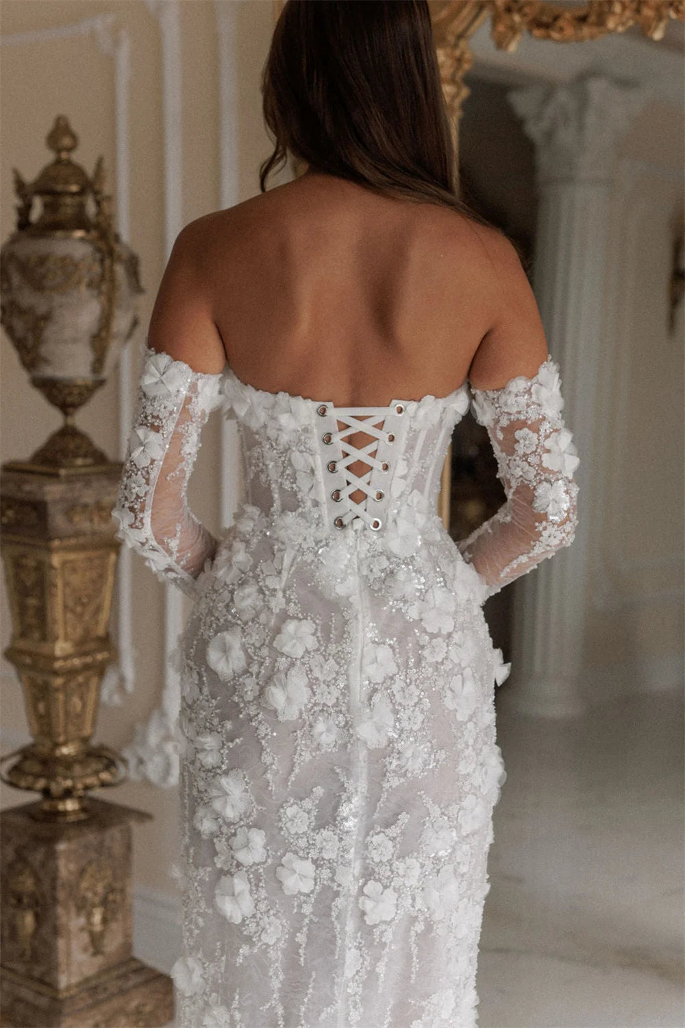 Woman wearing a white lace dress with long sleeves in an elegant interior setting.