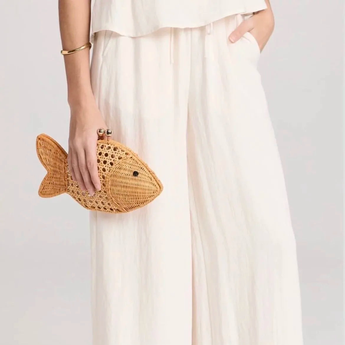 Person holding a woven fish-shaped clutch bag against a plain background