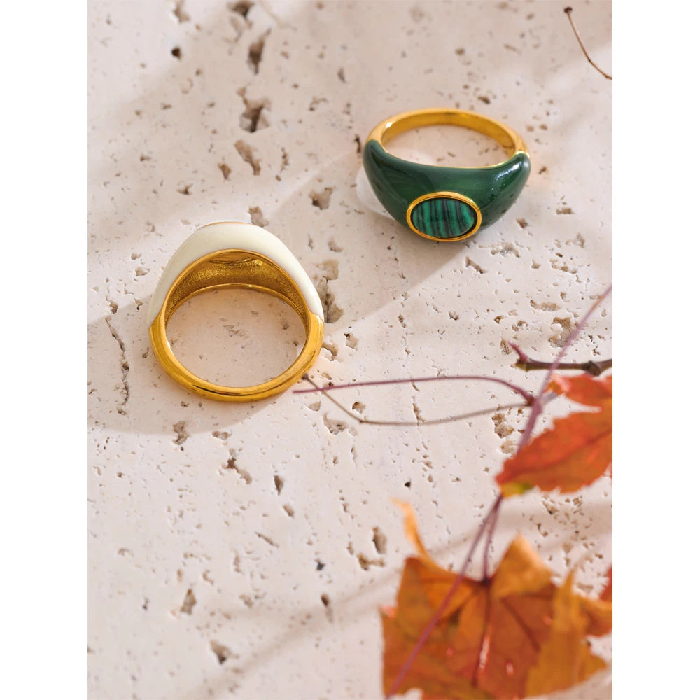 Two rings, one gold and one green, on a textured surface with autumn leaves.