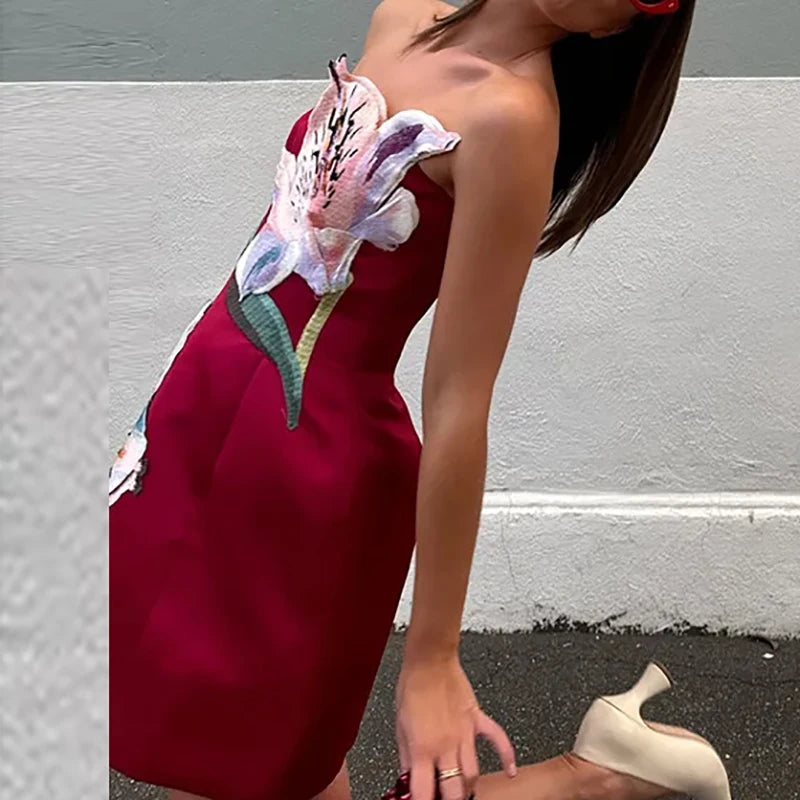 Woman wearing a red dress with floral designs against a gray wall.