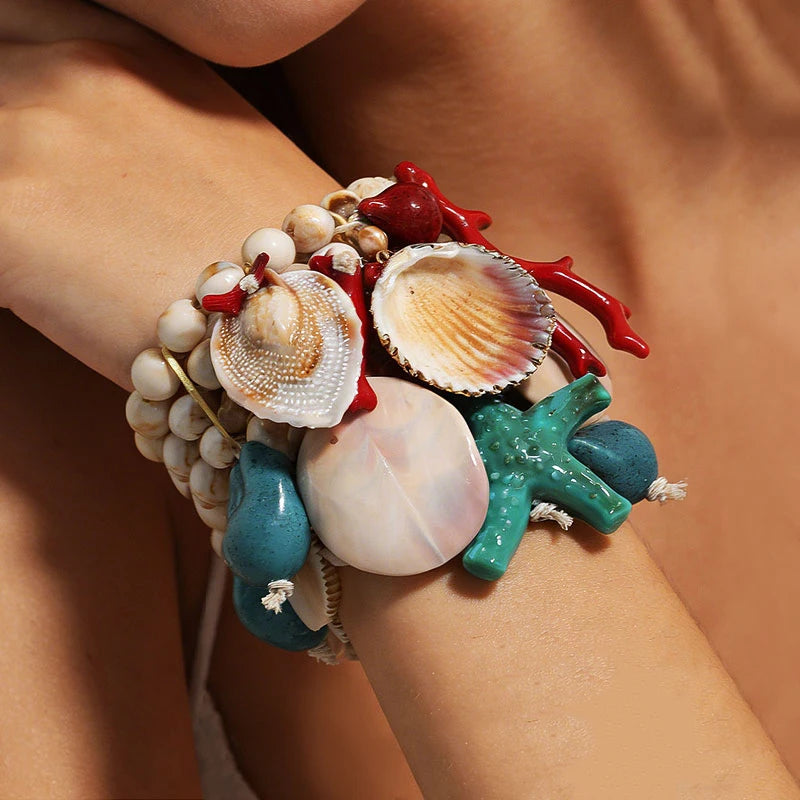 Bracelet with seashells, coral, and starfish on a wrist against a skin-toned background