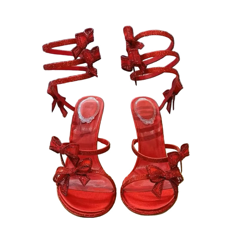 Red high-heeled sandals with bow details on a reflective surface