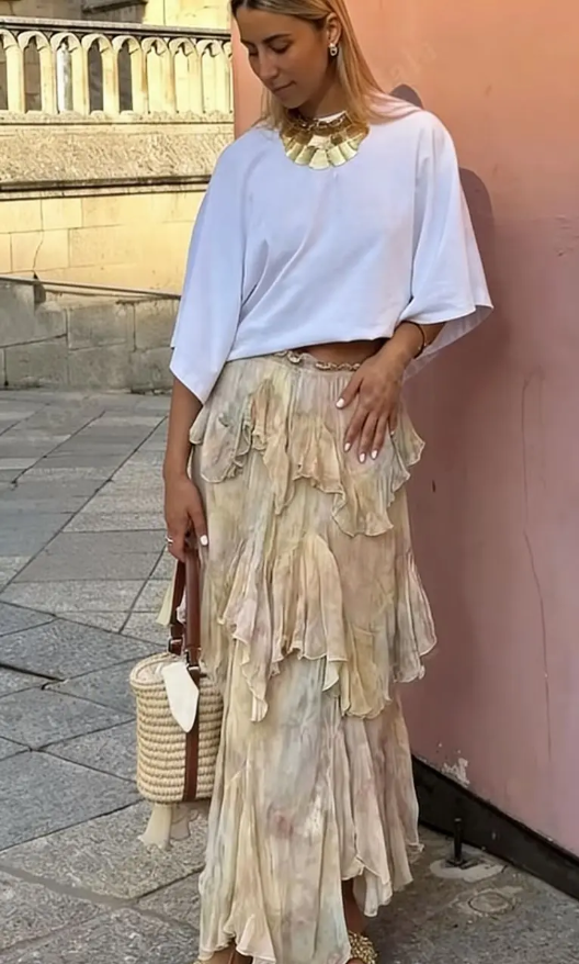 Woman wearing a white top and floral skirt with a pink wall and steps in the background